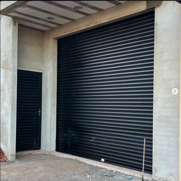 Porta de enrolar preta em galpão com porta social